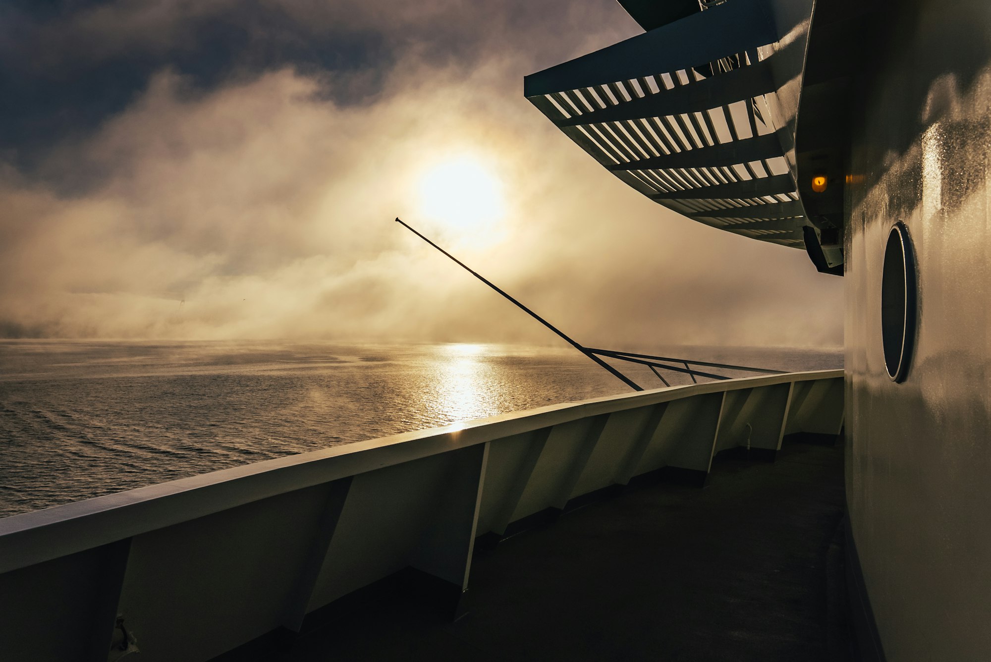 Sun setting over a misty ocean seen from a ship deck